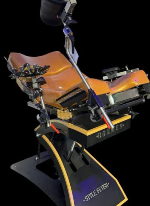 Ein spezieller brauner und schwarzer verstellbarer Stuhl mit mehreren Metallbefestigungen, beschriftet mit "Style Fetish", vor einem schwarzen Hintergrund.